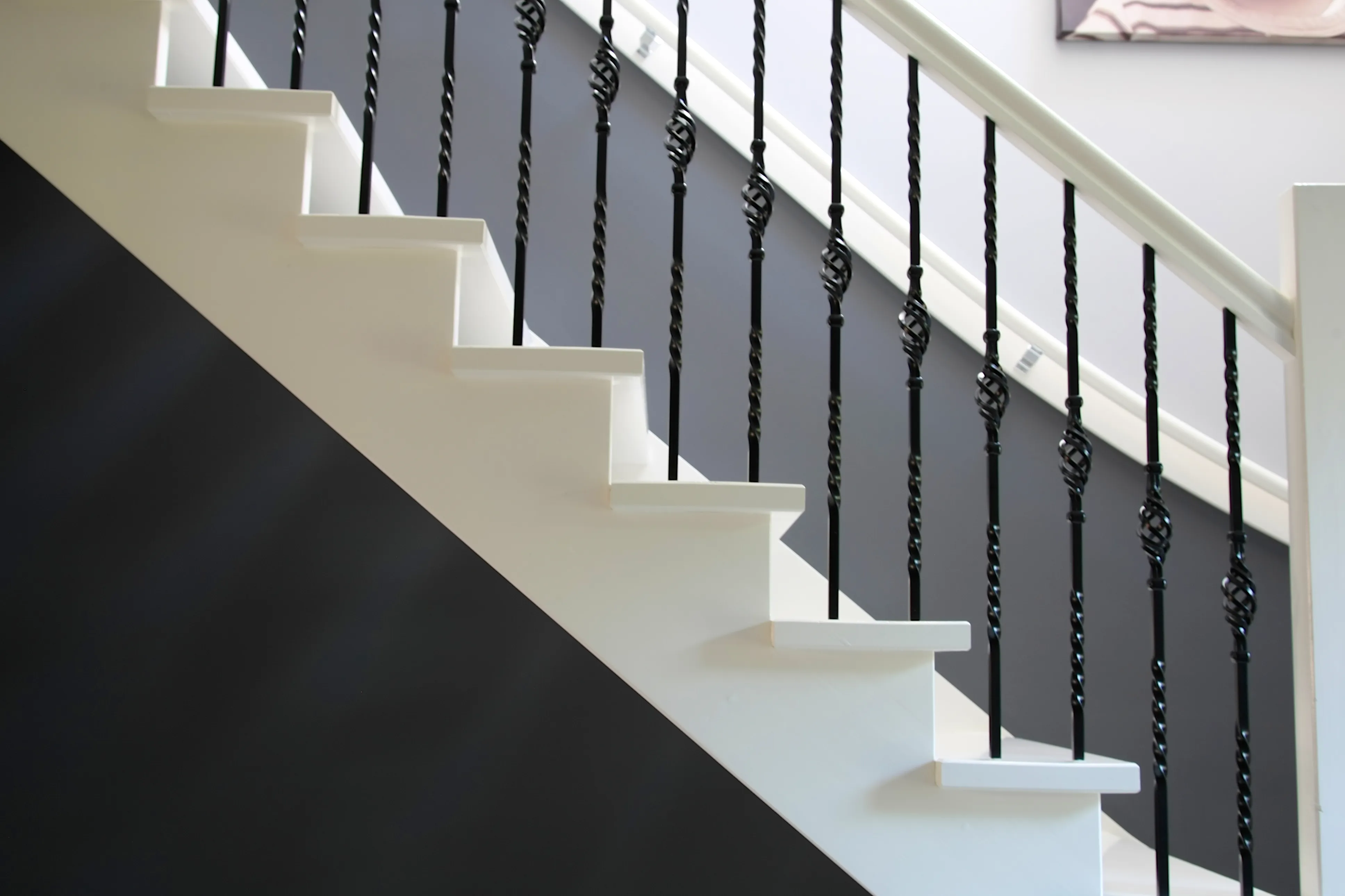 Witgelakte trap met smeedijzeren spijlen tegen een antracietkleurige wand.
