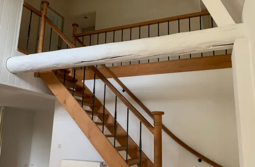 Houten trap met een eiken leuning en zwart metalen spijlen, naast strak wit schilderwerk.