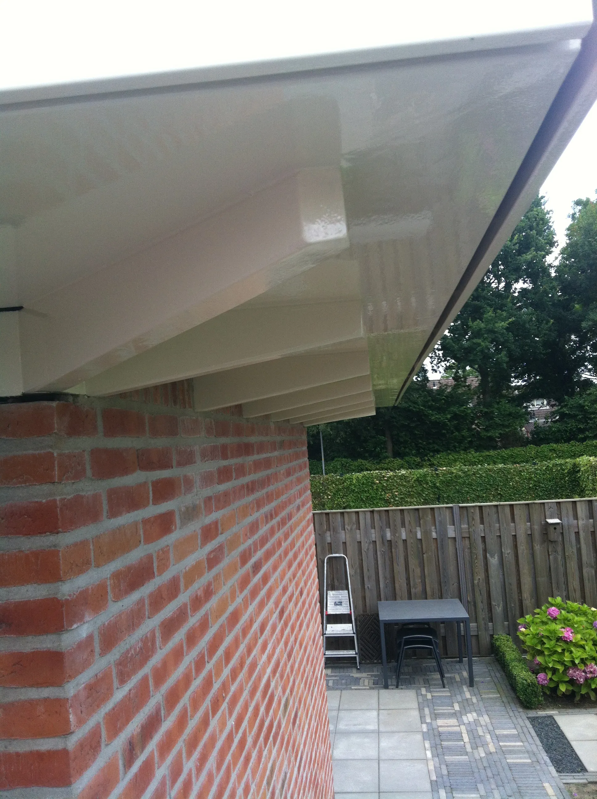Geschilderd boeideel en houtwerk onder een overkapping bij een bakstenen gevel.