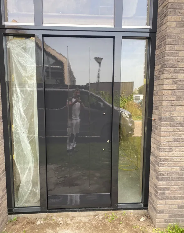 Veranda met glas en donker gelakte kozijnen aan de achterzijde van een woning.