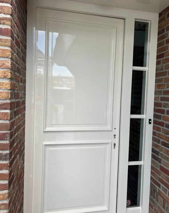 Witte voordeur, strak afgelakt in een bakstenen gevel.