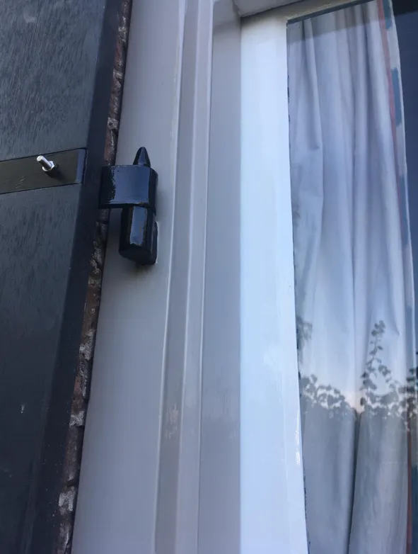 Detail van een wit gelakt kozijn met een donkere luikvanger.