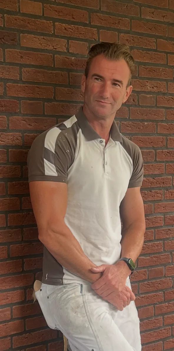 Dave Onkenhout, oprichter van Onkenhout Schilderwerken, tegen een bakstenen muur.