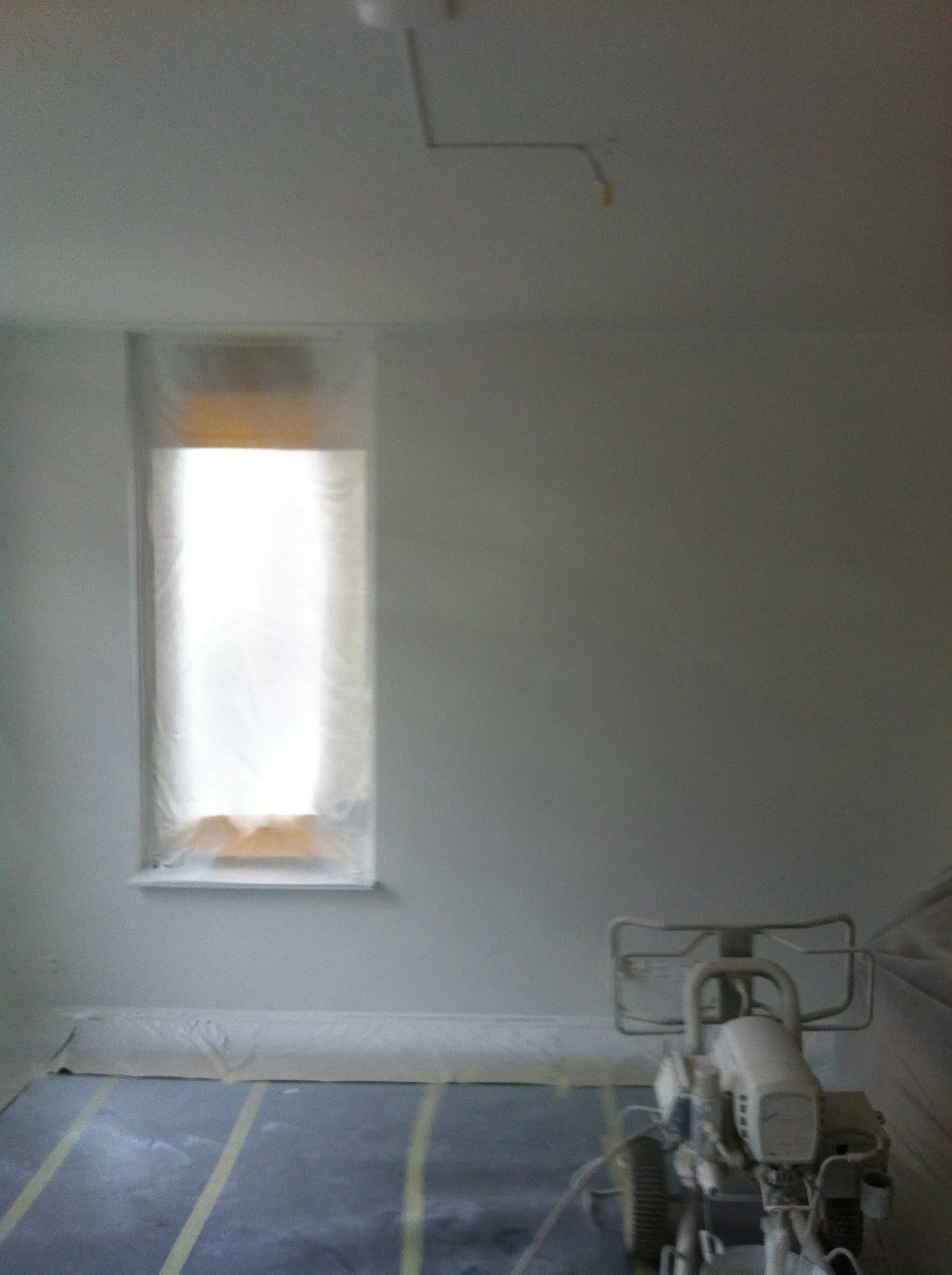 Gespoten wanden en plafond in een slaapkamer; het raam zit nog in het beschermfolie.